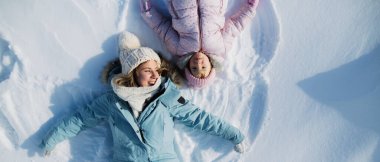 Top view portrait of cheerful mother with small daughter lying in snow in winter nature. clipart