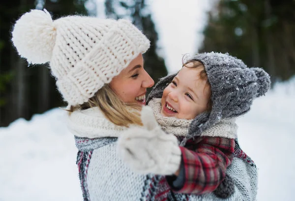 Alegre madre con pequeña hija de pie en la naturaleza de invierno, riendo. —  Fotos de Stock