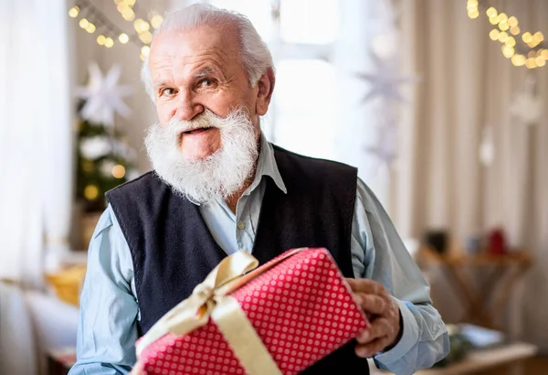 Vue de face de l'homme âgé heureux avec boîte cadeau à l'intérieur à la maison à Noël. — Photo