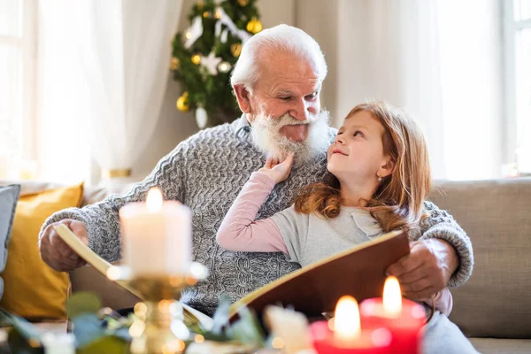 Menina pequena com avô sênior em casa em casa no Natal, olhando para fotografias. — Fotografia de Stock