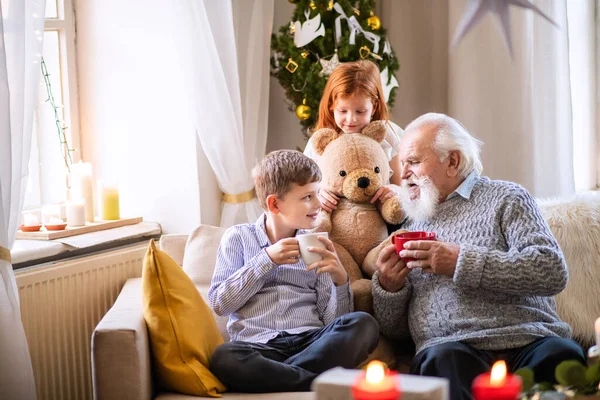 Crianças pequenas com avô sênior em casa no Natal, sentado e conversando. — Fotografia de Stock