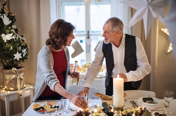 Feliz casal sênior dentro de casa, colocando a mesa no Natal. — Fotografia de Stock