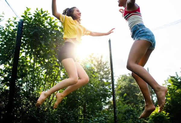 Low angle view of young teenager girls friends outdoors in garden, jumping on trampoline. — Stock Photo, Image