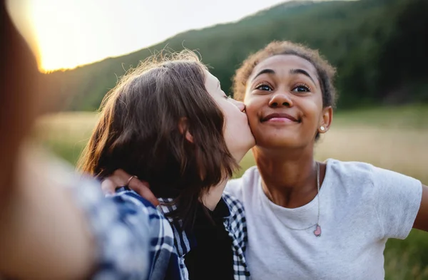 Vista frontal de jóvenes adolescentes amigas besándose al aire libre en la naturaleza, tomando selfie. — Foto de Stock