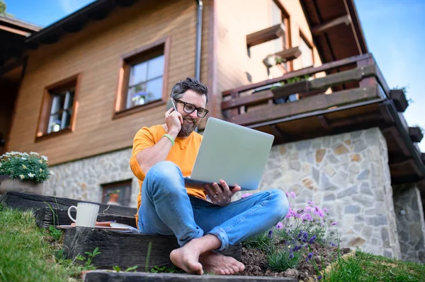 Homme mûr avec ordinateur portable et smartphone travaillant à l'extérieur dans le jardin, concept de bureau à domicile. — Photo