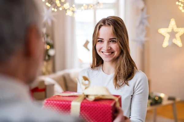 Jonge vrouw geeft cadeau aan onherkenbare grootvader binnen met Kerstmis. — Stockfoto