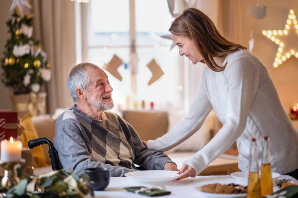 Mujer joven con abuelo mayor en silla de ruedas en casa en Navidad. — Foto de Stock