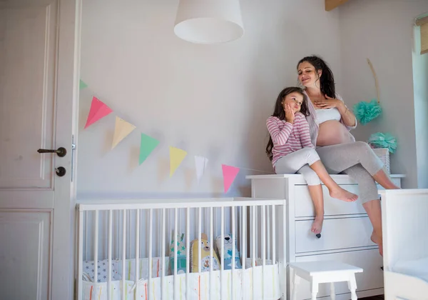 Portrait de femme enceinte avec une petite fille à l'intérieur à la maison, assise sur la commode. — Photo