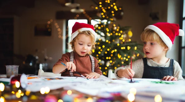 Portrait of small girl and boy indoors at home at Christmas, painting pictures. — Stock Photo, Image