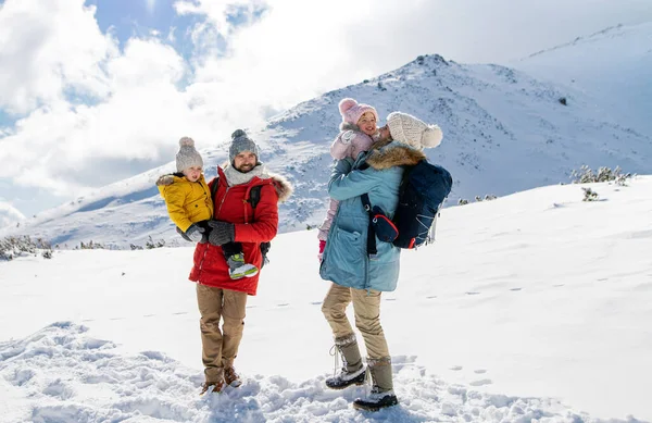Padre y madre con dos niños pequeños en la naturaleza invernal, de pie en la nieve. —  Fotos de Stock
