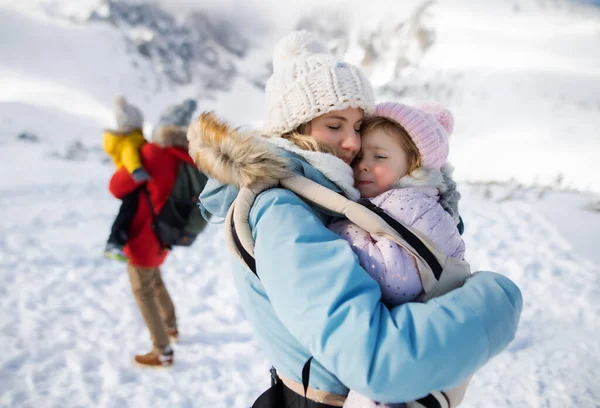 Mor med glad liten dotter i bärare stående i vinternaturen, vila. — Stockfoto
