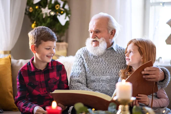 Petits enfants avec grand-père aîné à l'intérieur à la maison à Noël, en regardant des photos. — Photo