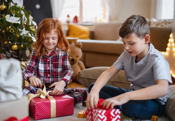 Menina pequena e menino de pijama em casa em casa no Natal, abrindo presentes. — Fotografia de Stock