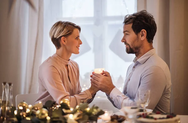 Vista lateral do casal feliz dentro de casa na mesa celebrando o Natal. — Fotografia de Stock
