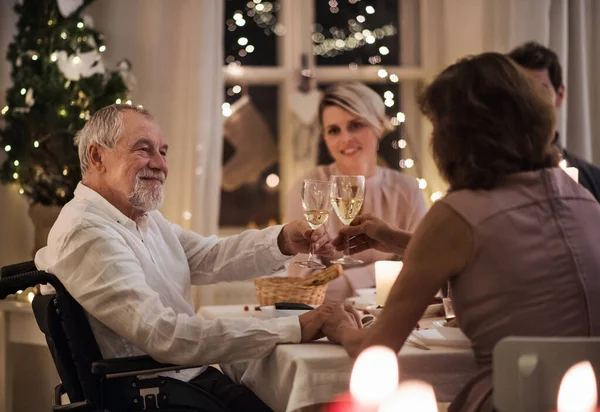 Homem sênior em cadeira de rodas com família dentro de casa celebrando o Natal juntos. — Fotografia de Stock