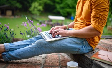 Diz üstü bilgisayarı olan tanınmayan bir adam bahçede çalışıyor, ev ofis konsepti..