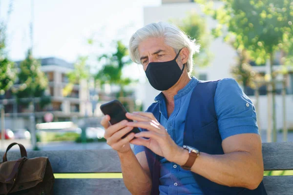 Портрет взрослого мужчины в маске для лица, сидящего на улице в городе, коронавирусная концепция. — стоковое фото