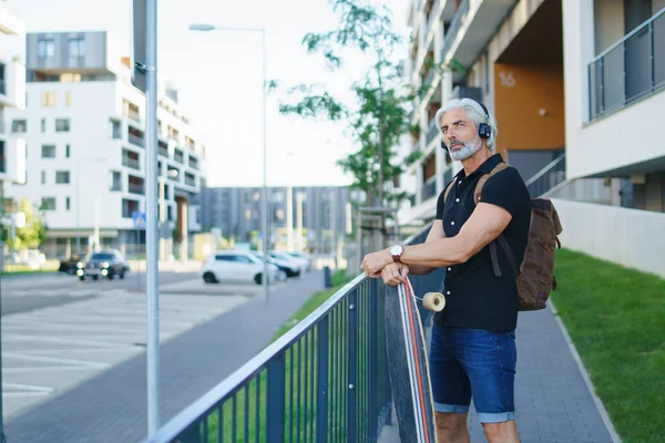 Портрет взрослого мужчины со скейтбордом на открытом воздухе в городе, возвращающегося к работе. — стоковое фото
