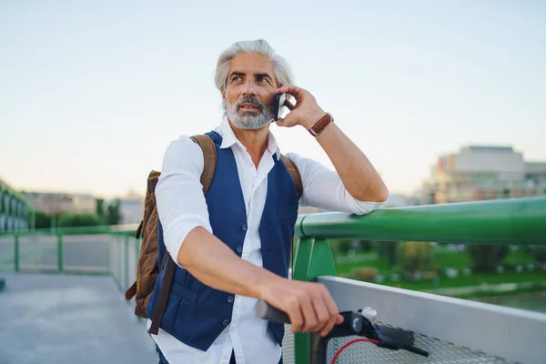 Retrato de hombre maduro con scooter eléctrico al aire libre en la ciudad, usando teléfono inteligente. —  Fotos de Stock