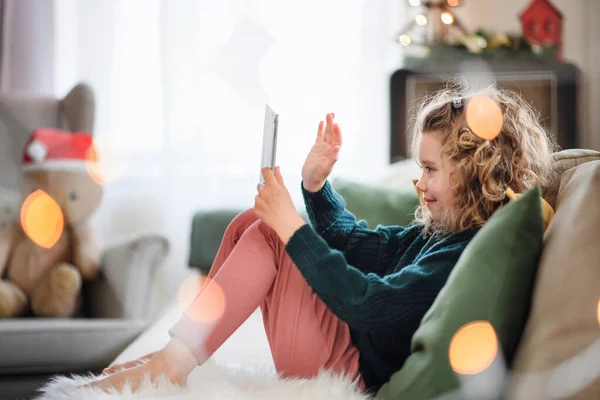 Niña pequeña con tableta sentada en casa en Navidad, teniendo videollamada. — Foto de Stock