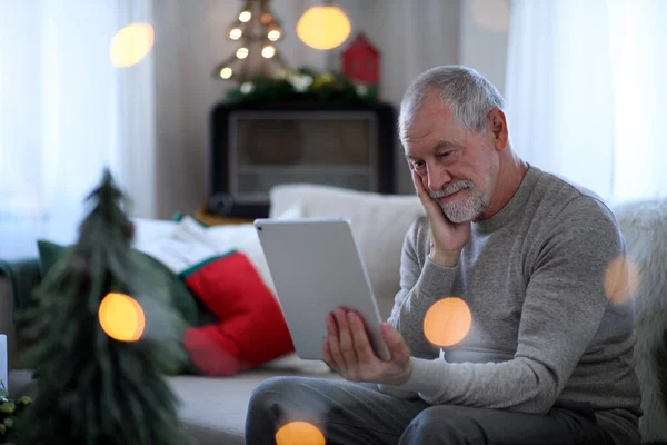 Сумний і самотній старший чоловік з планшетом сидить за столом в приміщенні на Різдво, концепція самотності . — стокове фото