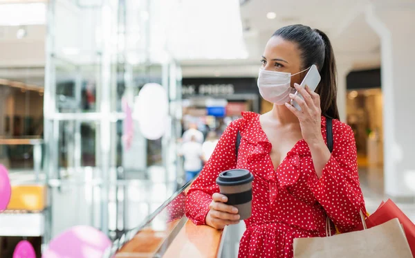 Женщина в маске для лица стоит и использует смартфон в помещении в торговом центре, коронавирус концепции. — стоковое фото