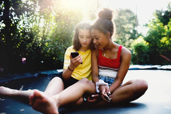 Вид спереду молодих дівчат-підлітків друзів на відкритому повітрі в саду, використовуючи смартфон . — стокове фото