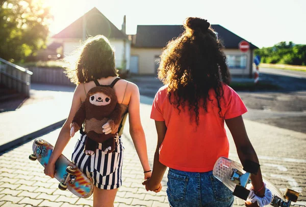 Widok z tyłu nastolatki dziewczyny przyjaciół z deskorolkami na zewnątrz w mieście. — Zdjęcie stockowe