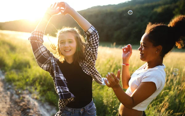 Young teenager girls friends outdoors in nature at sunset, blowing bubbles. — Stock Photo, Image