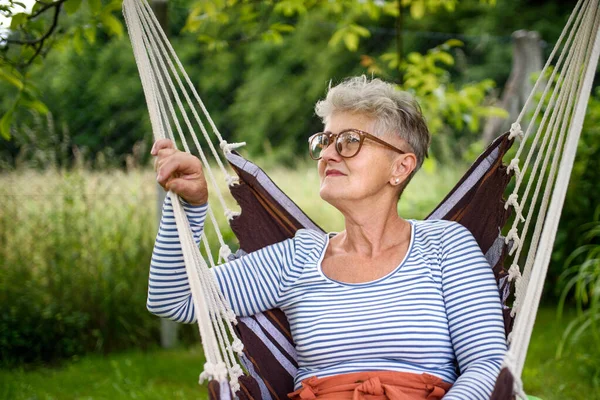Portret szczęśliwej starszej kobiety siedzącej na świeżym powietrzu na wiszącym krześle huśtawkowym w ogrodzie, relaksujący. — Zdjęcie stockowe