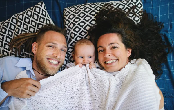 Fiatal pár baba lánya pihen a takaró alatt, nézi a kamerát. — Stock Fotó