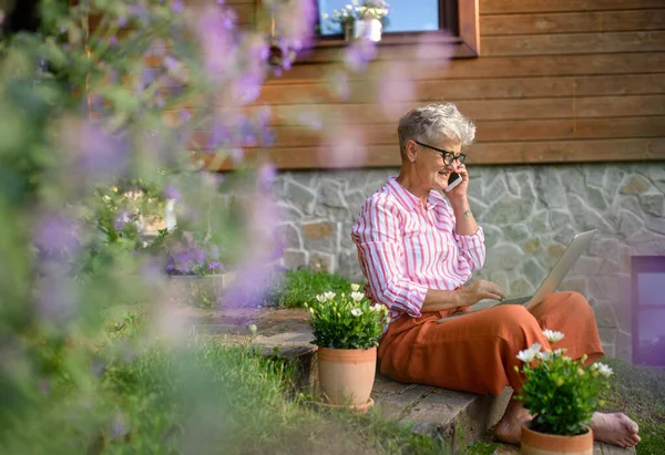 Старша жінка з ноутбуком і смартфоном, що працює на відкритому повітрі в саду, концепція домашнього офісу . — стокове фото