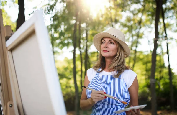 Portrait of mature woman with pallete painting outdoors in garden. — Stock Photo, Image