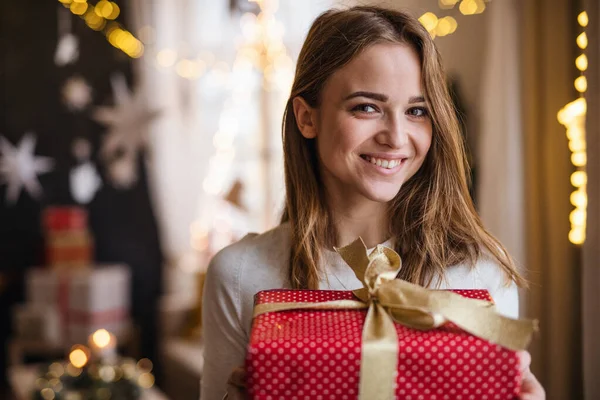 Happy young woman indoors at home at Christmas, holding present. — Stock Photo, Image
