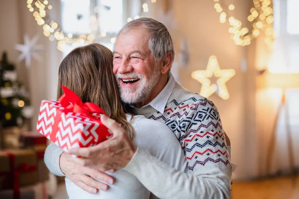 Jeune femme donnant cadeau à heureux grand-père à l'intérieur à la maison à Noël. — Photo