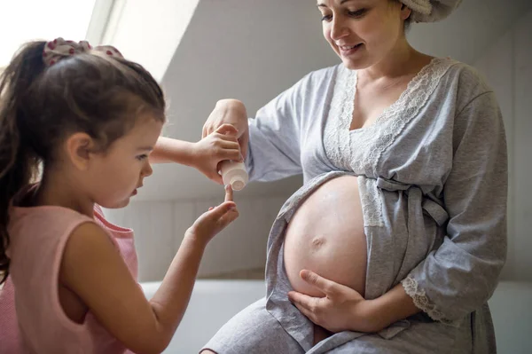 Маленькая девочка сливает живот беременной матери в помещении в ванной комнате дома. — стоковое фото