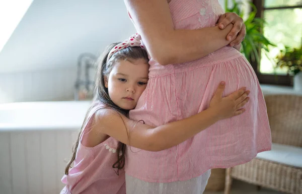 Portret ciężarnej kobiety z córeczką w domu, przytulanie. — Zdjęcie stockowe