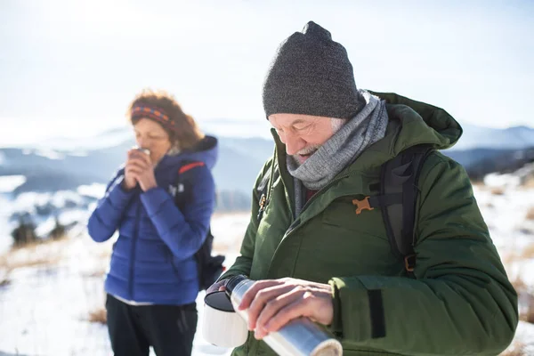 Senderistas pareja de ancianos en la naturaleza de invierno cubierto de nieve, beber té caliente. — Foto de Stock