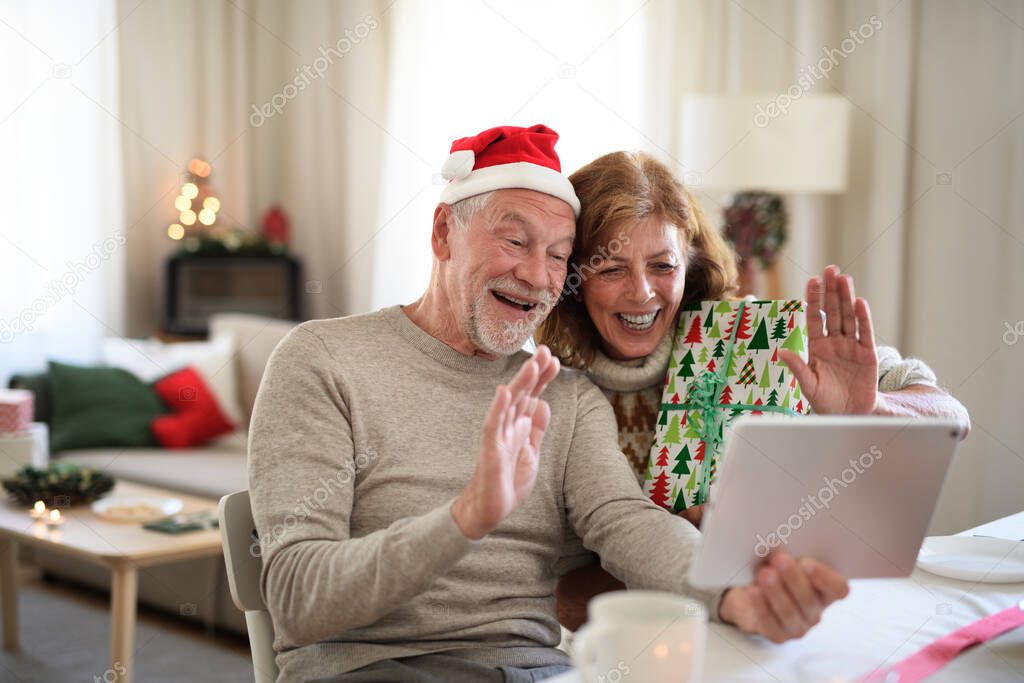 Front view of senior couple indoors at home at Christmas, having video call with family.