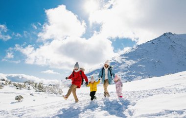 Anne ve baba kışın iki küçük çocukla karda yürüyorlar..