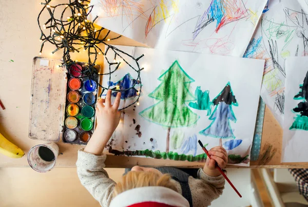 Top view of unrecognizable small child indoors at home at Christmas, painting pictures. — Stock Photo, Image