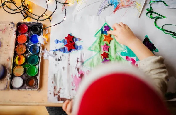 Horní pohled na nepoznatelné malé dítě doma na Vánoce, malování obrázků. — Stock fotografie