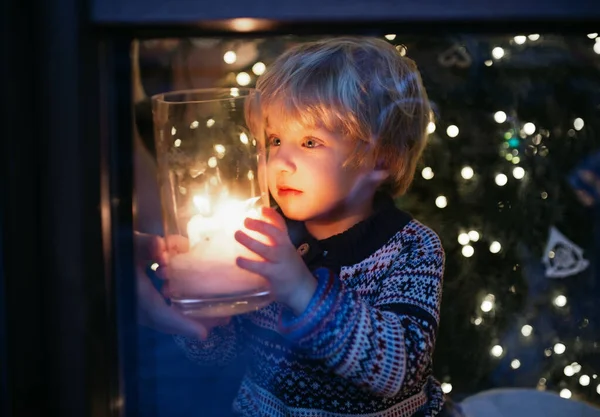 Portret małego chłopca w domu na Boże Narodzenie, trzymającego świecę w nocy. — Zdjęcie stockowe