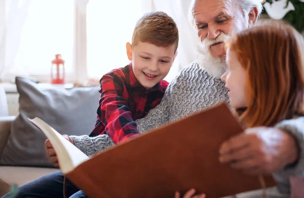 Niños pequeños con abuelo mayor en casa en Navidad, mirando fotografías. — Foto de Stock