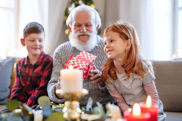 Malé děti se starším dědečkem doma o Vánocích, držící dárky. — Stock fotografie