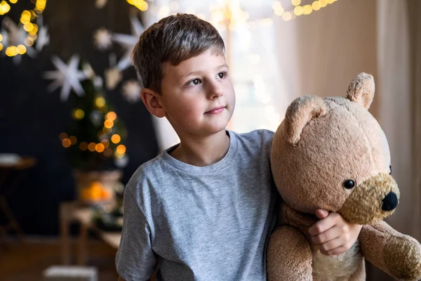Small boy indoors at home at Christmas, holding teddy bear. — Stock Photo, Image