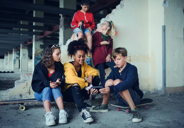 Sekelompok remaja geng duduk di dalam gedung yang ditinggalkan, menggunakan smartphone. — Stok Foto