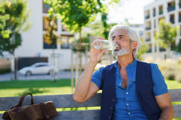 Портрет зрелого мужчины, сидящего на улице в городе, с питьевой водой. — стоковое фото