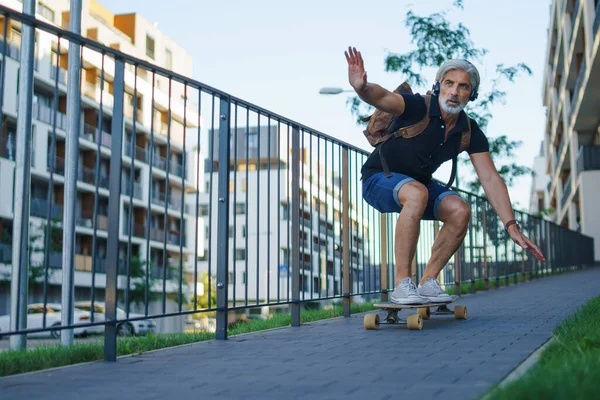 Portrait d'homme mature chevauchant le skateboard à l'extérieur en ville, retournant au travail. — Photo
