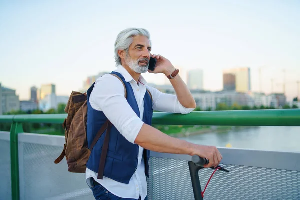 スマートフォンを使用して、都市の屋外で電動スクーターと成熟した男の肖像画. — ストック写真